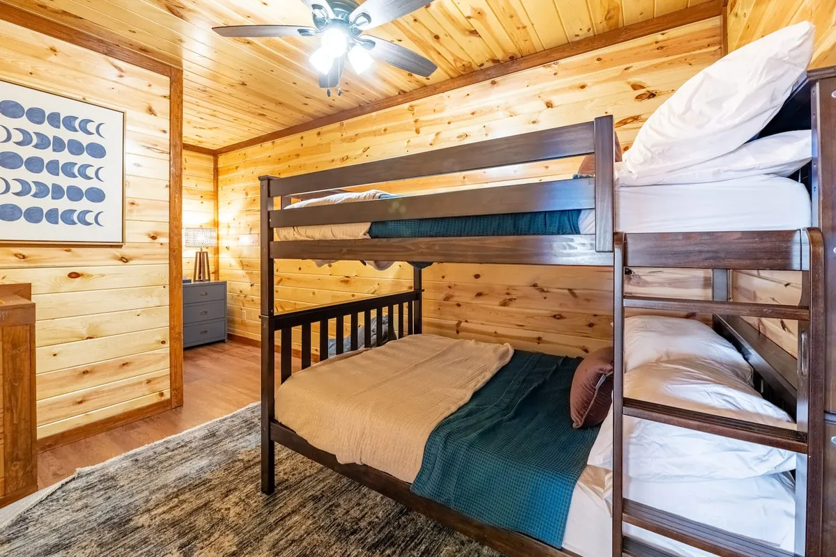 A cozy, kid-friendly bedroom with charming wooden paneling, featuring sturdy bunk beds dressed in plush comforters. Above the beds, moon phase artwork adds a whimsical touch, making the space ideal for families and playful sleepovers.