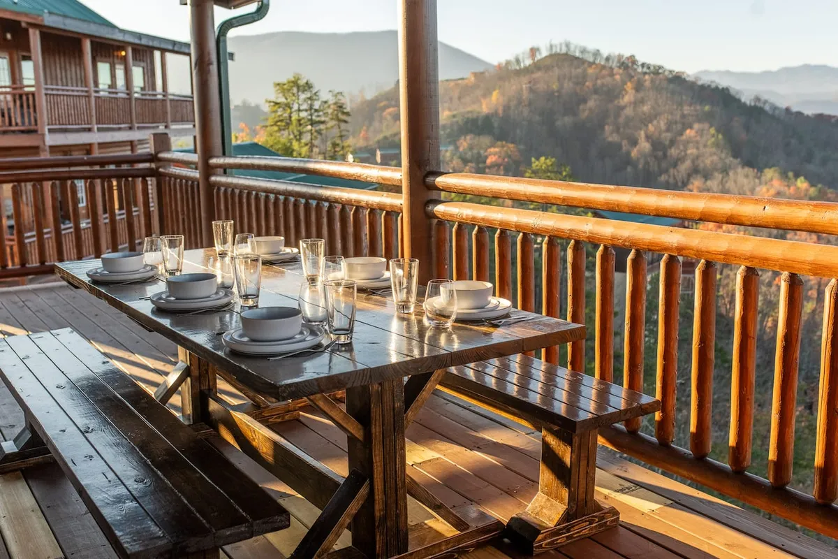 A wooden outdoor dining table is set for a meal with table settings, all positioned to take in expansive mountain views. The relaxed atmosphere is ideal for social gatherings, morning coffee, or sunset dinners in nature.
