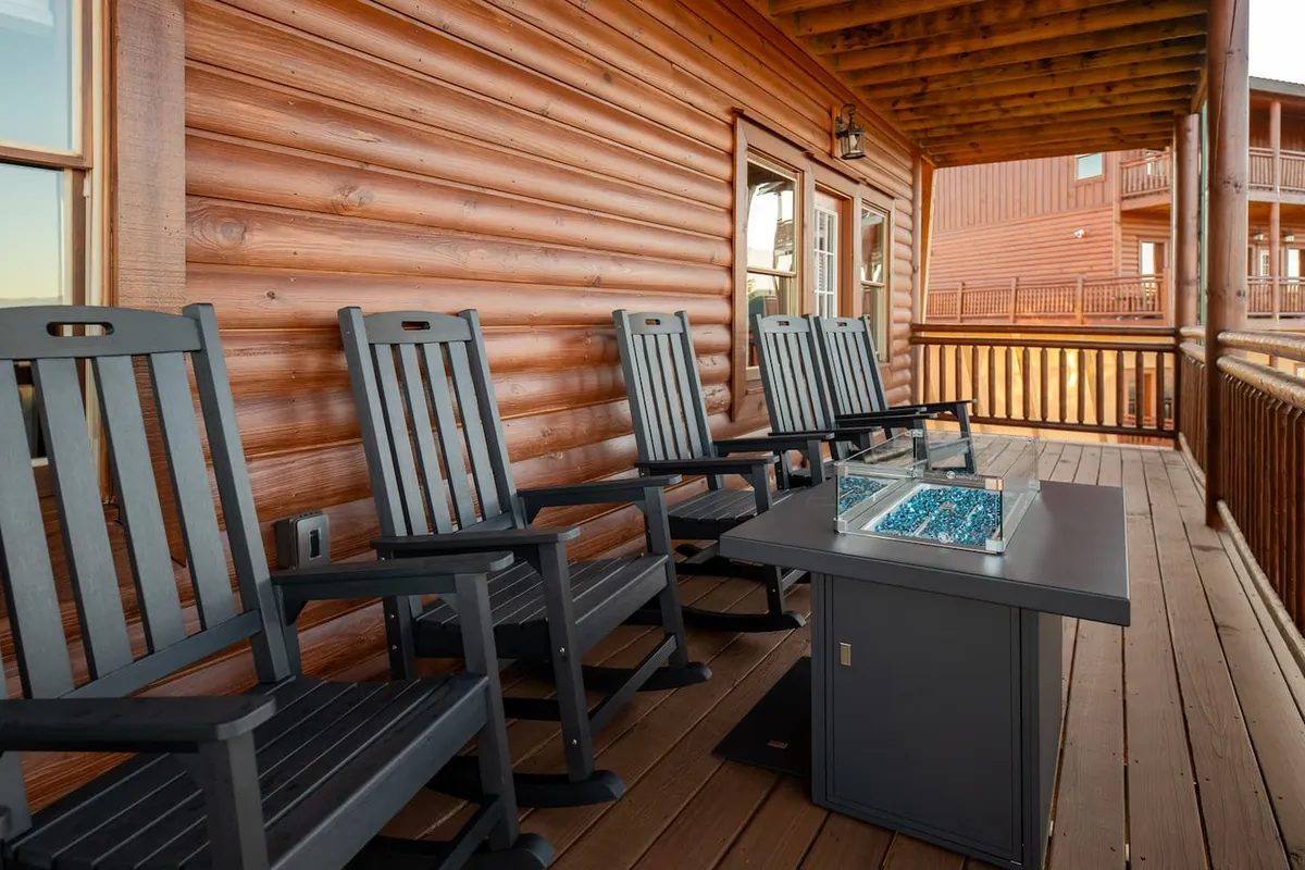A welcoming exterior deck featuring classic wooden rocking chairs, a glass table adorned with decorative stones, and sturdy log railings. The scene suggests a cozy, pet-friendly space perfect for relaxing with a dog while enjoying scenic mountain views and fresh air.