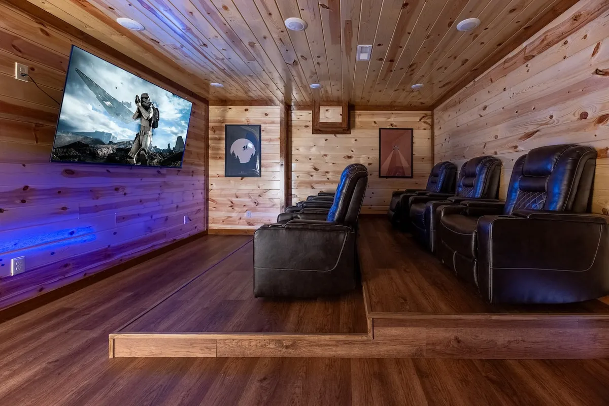 A cozy private theater room with plush reclining chairs, a large television screen, and stylish wooden paneling complemented by tasteful artwork. The setup is ideal for immersive movie nights or gaming sessions with friends or couples.