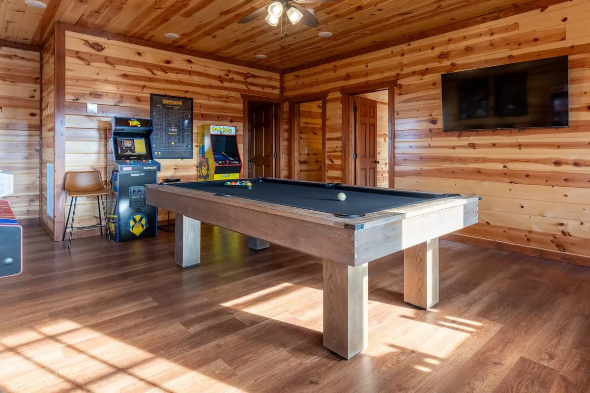 A lively game room showcasing a pool table, classic arcade machines, and a television screen. The space is infused with energy, ideal for friendly competitions and playful memories.