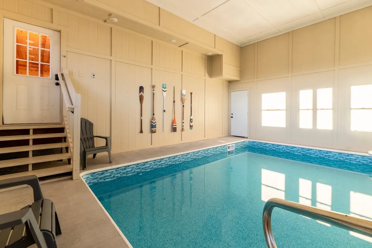 A fresh angle of the indoor pool space, showing the pool, decorative wall paddles, and a set of stairs leading to the outdoors. The area is bathed in natural light, enhancing the inviting, serene feeling and suggesting easy movement between indoor relaxation and outdoor views.
