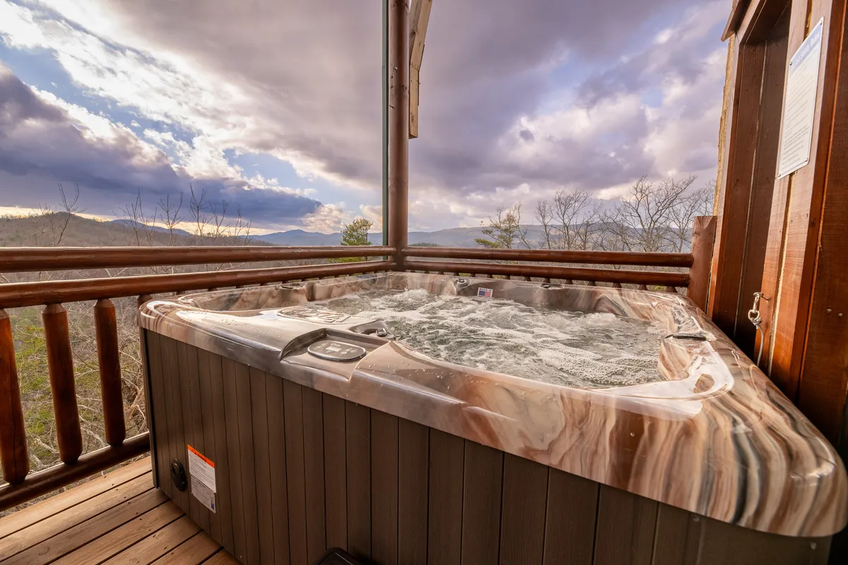 An exterior hot tub with a stunning mountain view, bordered by a rustic wooden railing. The hot tub is positioned for maximum privacy and scenic enjoyment, creating an idyllic spot for unwinding after a day of adventure.